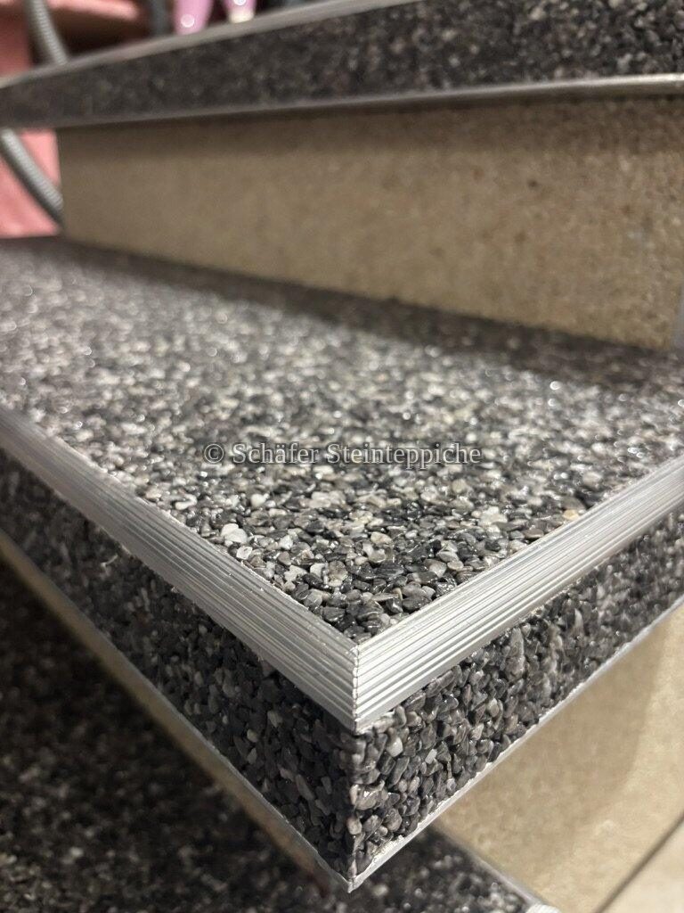 Nahaufnahme einer dunkelgrauen Steinteppich-Treppenkante mit Aluminiumprofil